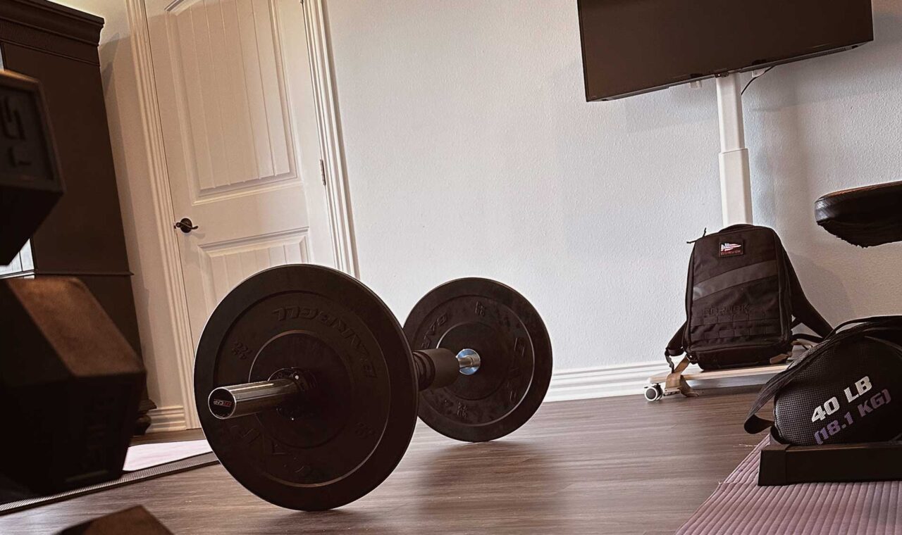 home gym setup with dumbbells, barbell, bench, and yoga mat